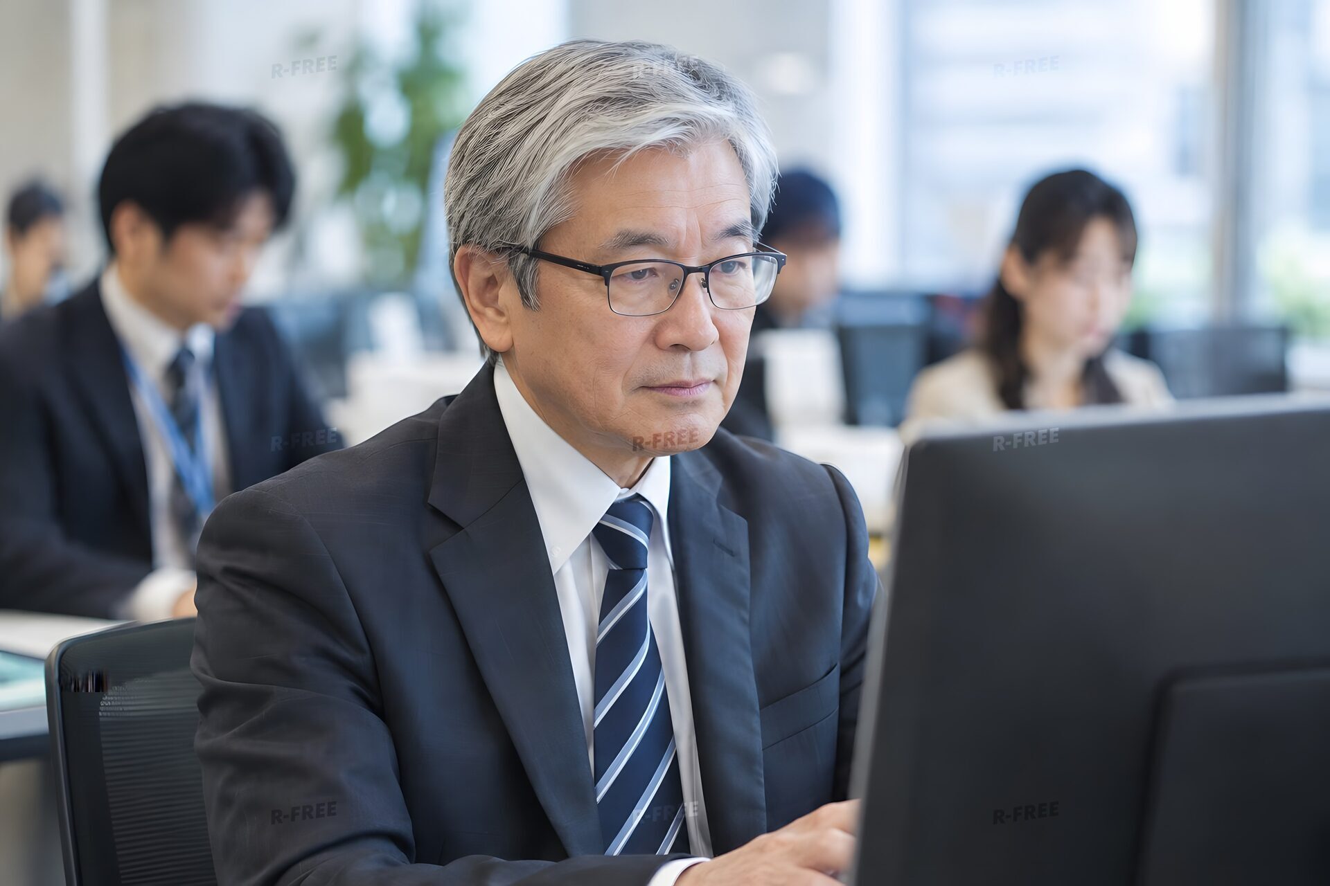オフィスでパソコンに向かう白髪の60代男性社員