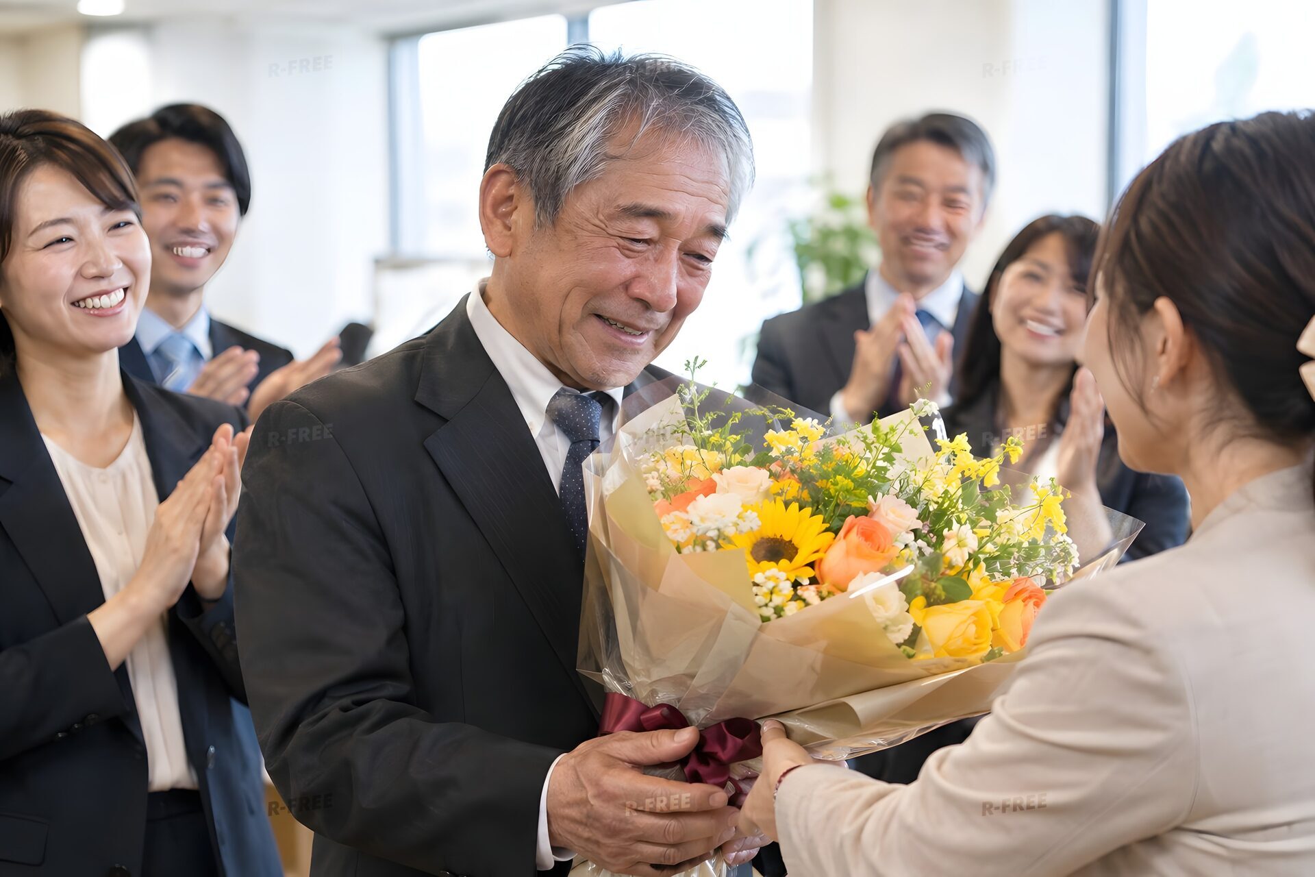 定年退職の日に同僚から花束を受け取る60代男性