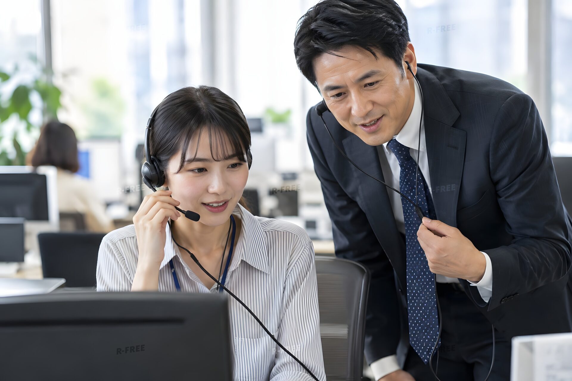 若手の電話営業を横で聞いて指導する40代の営業マネージャー