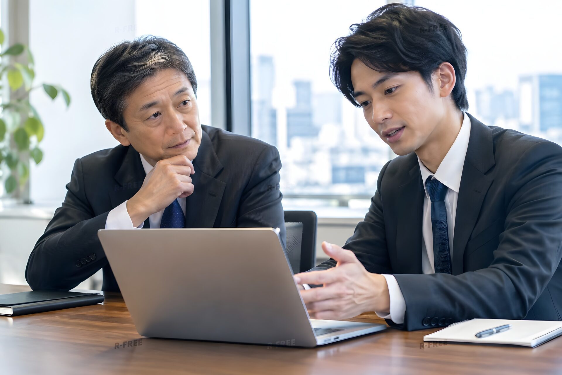 若手社員からノートパソコンでAIツールの説明を受ける50代の役員