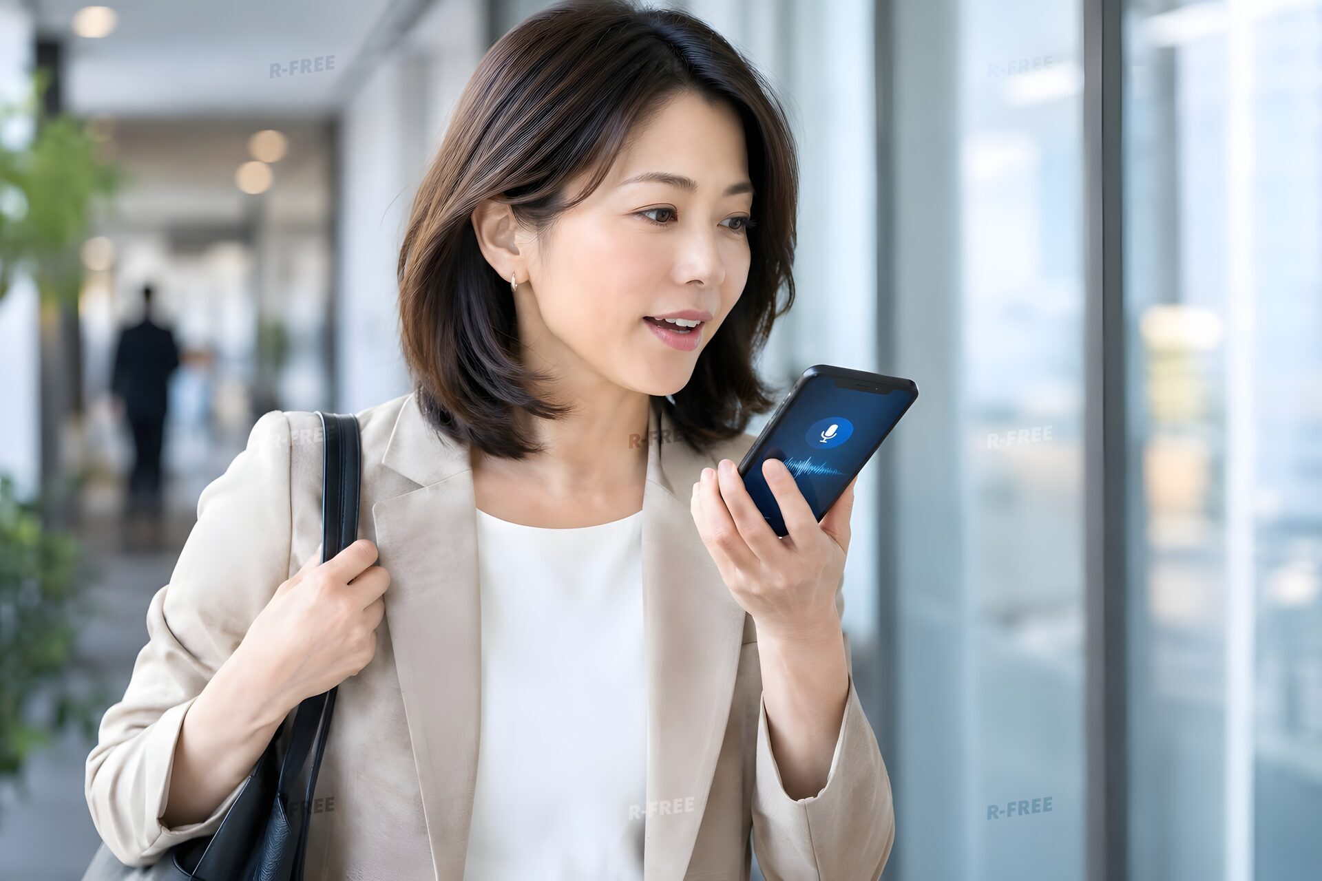 オフィスの廊下で歩きながらスマートフォンの音声AIに話しかける40代女性