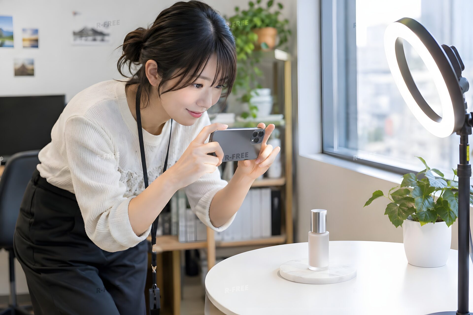 リングライトの下でスマートフォンで商品を撮影する20代のSNS担当者