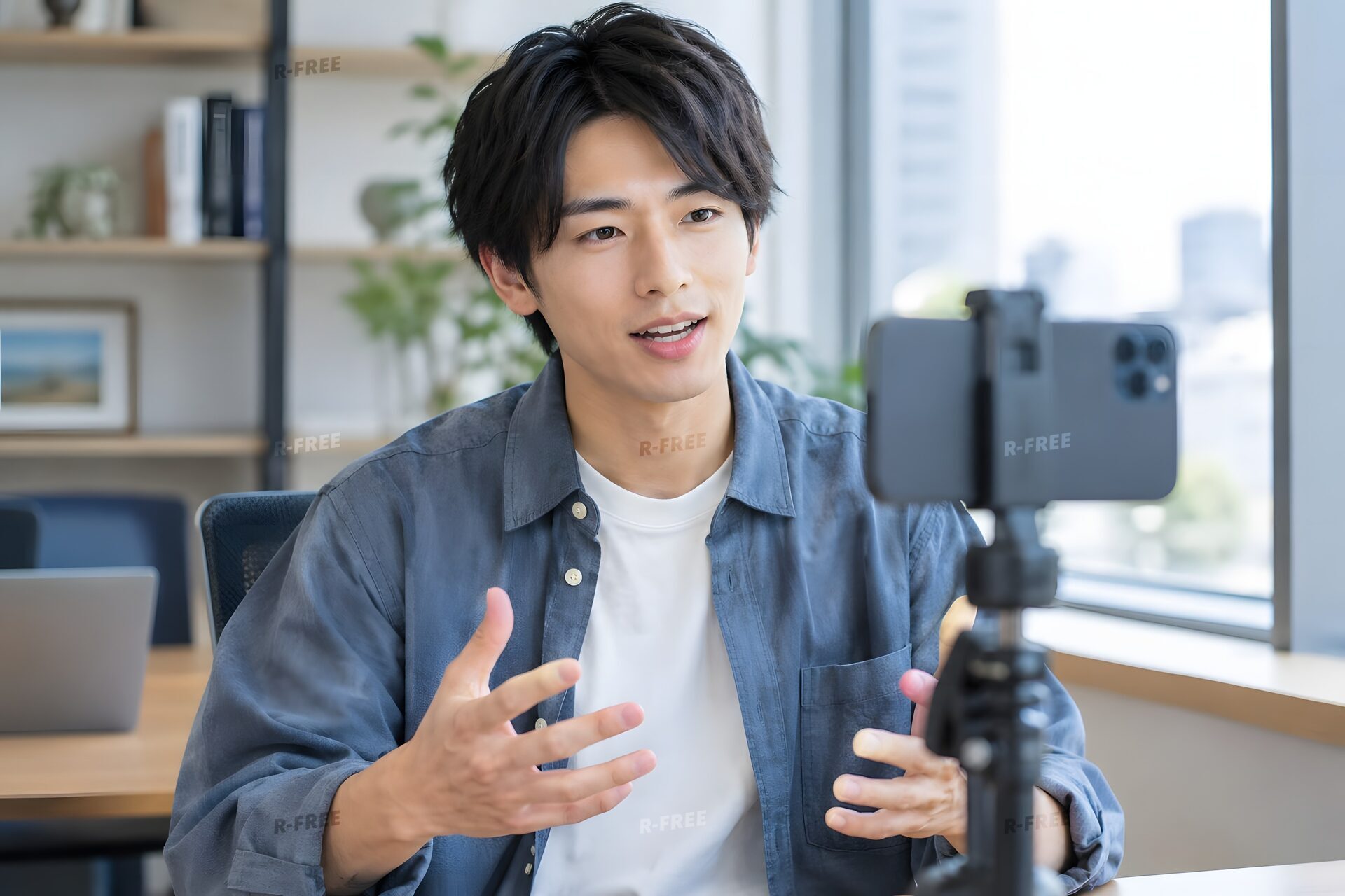 オフィスで三脚に立てたスマートフォンに向かって縦動画を撮る20代男性