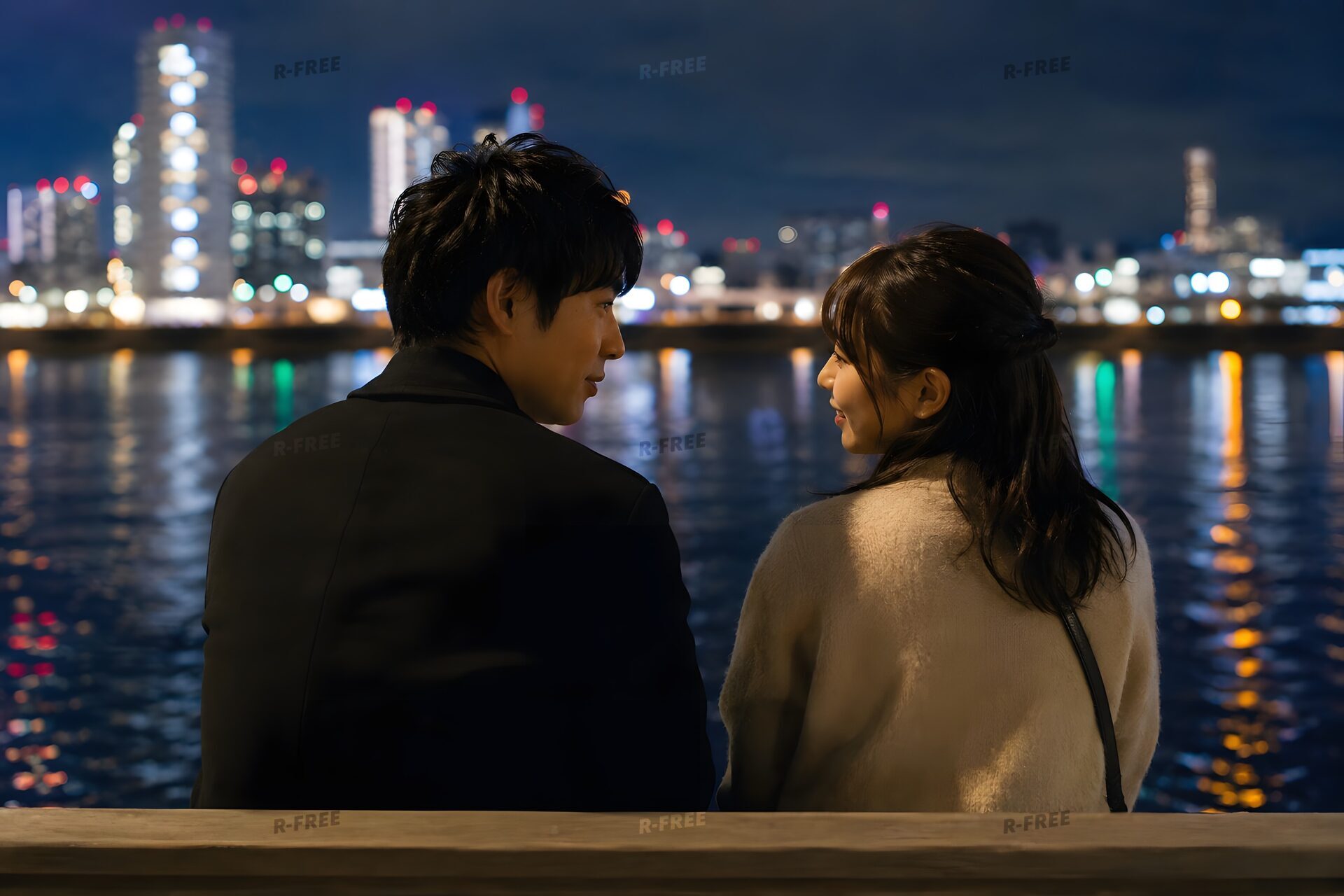 水辺のベンチで夜景を見るカップル