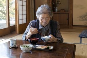 静かな和室で一人で食事をする高齢女性
