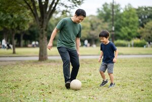 公園で息子にボールの蹴り方を教える父親