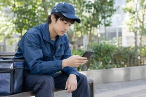 休憩中にスマホで仕事を探す20代の配達員