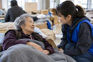 避難所で高齢女性に声をかけるボランティア