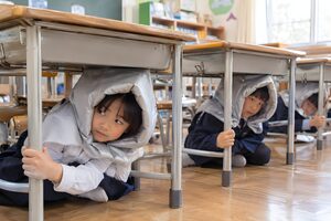 机の下に隠れる避難訓練の小学生