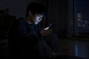 暗い部屋でスマホを見る20代男性