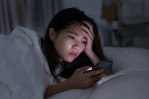 ベッドでスマホを見て思い詰める20代女性