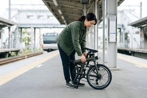 駅のホームで折りたたみ自転車を畳む女性