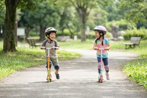 ヘルメットで並んでキックスクーターに乗る子ども
